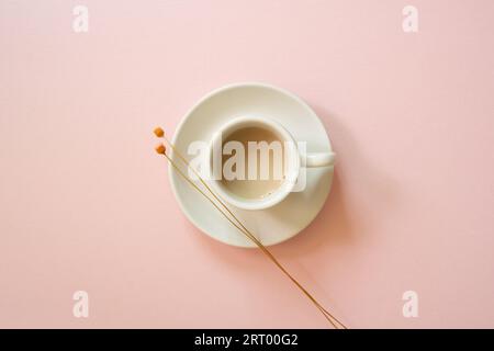 Tasse blanche de café avec fleur sèche sur fond rose. vue de dessus Banque D'Images