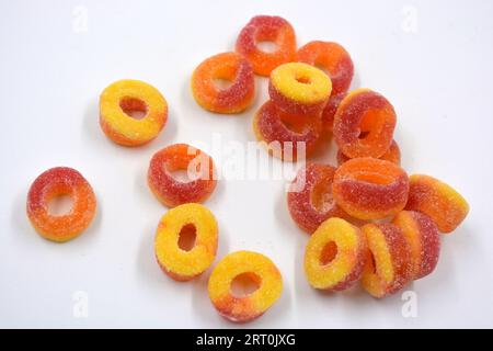 De beaux bonbons colorés et lumineux sous la forme de beignets orange et rouges en poudre de sucre, disposés sur un fond blanc mat. Banque D'Images