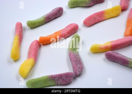 Bonbons colorés beaux et lumineux de bonbons pour enfants sous la forme de vers de terre sucrés de différentes couleurs disposés sur un fond blanc mat. Banque D'Images