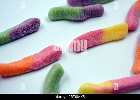 Bonbons colorés beaux et lumineux de bonbons pour enfants sous la forme de vers de terre sucrés de différentes couleurs disposés sur un fond blanc mat. Banque D'Images