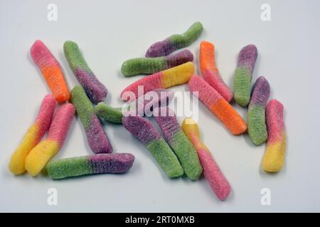 Bonbons colorés beaux et lumineux de bonbons pour enfants sous la forme de vers de terre sucrés de différentes couleurs disposés sur un fond blanc mat. Banque D'Images