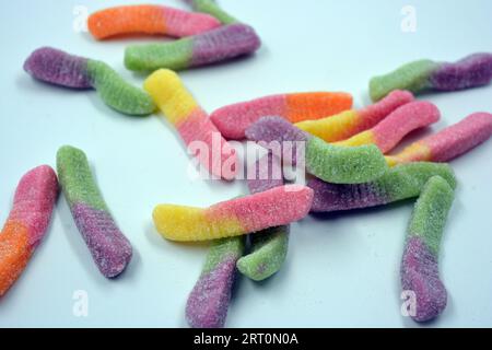 Bonbons colorés beaux et lumineux de bonbons pour enfants sous la forme de vers de terre sucrés de différentes couleurs disposés sur un fond blanc mat. Banque D'Images