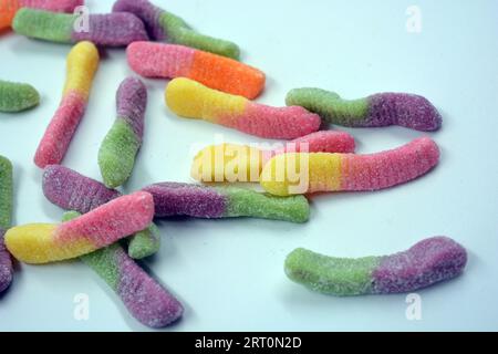 Bonbons colorés beaux et lumineux de bonbons pour enfants sous la forme de vers de terre sucrés de différentes couleurs disposés sur un fond blanc mat. Banque D'Images