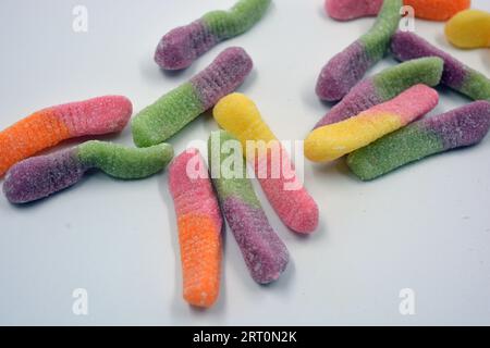 Bonbons colorés beaux et lumineux de bonbons pour enfants sous la forme de vers de terre sucrés de différentes couleurs disposés sur un fond blanc mat. Banque D'Images