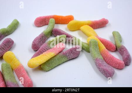 Bonbons colorés beaux et lumineux de bonbons pour enfants sous la forme de vers de terre sucrés de différentes couleurs disposés sur un fond blanc mat. Banque D'Images