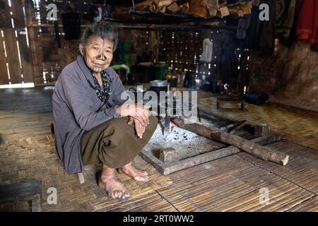 Femme locale de la tribu Apatani assise sur une petite chaise dans une maison traditionnelle en bois dans un petit village près de Ziro dans l'Arunachal Pradesh, Inde Banque D'Images