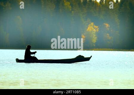 Waterman. Old Veps se déplace à travers le lac en bateau de bois de fortune, brouillard léger. Lac forestier dans les tons jaunes d'automne. Silhouette anonyme méconnue Banque D'Images