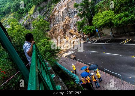 Un homme prend la vue pendant que les travailleurs élaborent une stratégie de nettoyage à un glissement de terrain qui a complètement bloqué Yiu Hing Road à Shau Kei WAN. Hong Kong a connu ses pluies les plus abondantes depuis le début des records, avec un signal d'avertissement de pluie noire en place pendant plus de 12 heures. Avec une pluie dépassant 70 mm par heure dans certaines zones, il y avait des rues inondées, des centres commerciaux et des stations MTR ainsi que des rapports de 39 glissements de terrain. Le Gouvernement a mis en place 15 refuges temporaires pour ceux qui en avaient besoin et les hôpitaux ont signalé que 144 patients avaient demandé un traitement médical. Banque D'Images