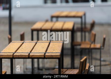 Les jours de pluie, les tables et chaises en bois vintage vides et humides sont situées dans le coin salon extérieur fermé du bar à hamburgers Banque D'Images