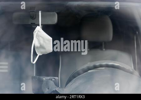 Masque de protection blanc suspendu au rétroviseur dans la voiture vu de l'avant par le bouclier avant Banque D'Images