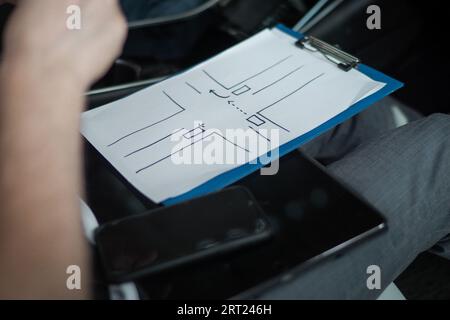 Instructeur de conduite masculin assis dans la voiture tout en tenant le dessin pendant le test dans l'école de conduite. Gros plan. Test de conduite, cours de conducteur, examen Banque D'Images