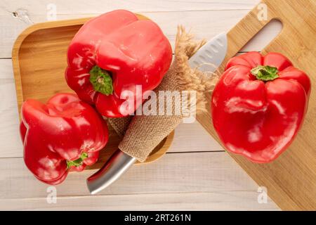 Trois poivrons rouges doux avec plateau en bambou, couteau et planche de cuisine en bois sur table en bois, macro, vue de dessus. Banque D'Images