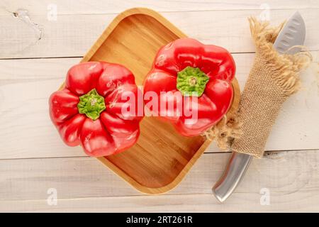 Deux poivrons rouges sucrés avec plateau en bambou, couteau sur table en bois, macro, vue de dessus. Banque D'Images