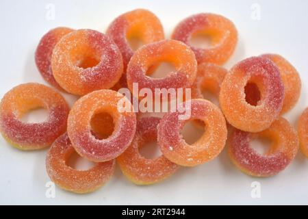 De beaux bonbons colorés et lumineux sous la forme de beignets orange et rouges en poudre de sucre, disposés sur un fond blanc mat. Banque D'Images