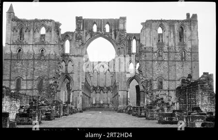 Abbaye de Rievaulx, Rievaulx, Ryedale, North Yorkshire, 1940-1948. Vue de la nef et du chœur prise de l'intérieur des ruines, avec de bas murs en gravats au premier plan et une ligne de vue nette à la fin de la nef. Au centre de l'image se trouve une énorme entrée voûtée à travers la nef qui est flanquée de chaque côté par des colonnes et trois étages d'arches. Plus à l'extérieur de ceux-ci se trouvent des sections de murs à trois étages, dont le plus haut a de la brique d'une couleur différente. À la toute fin se trouve un petit sommet pyramidal qui est légèrement plus haut que le reste du mur, mais cela n'est vu que sur t Banque D'Images