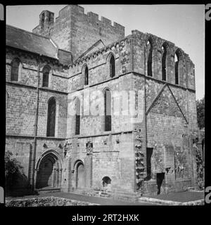 Lanercost Prieuré, Lanercost, Burtholme, Carlisle, Cumbria, 1940-1962. Vue extérieure des ruines du Prieuré de Lanercost, très probablement du côté sud. Le côté droit de l'image montre une section de trois étages de l'ancien prieuré, peut-être le transept sud, qui a une petite entrée en arc rond sur le côté ouest dans le coin, et une forme de triangle au-dessus du deuxième étage sur le côté sud. À droite se trouve la nef du prieuré, qui est encore utilisée comme église paroissiale, l'église Sainte-Marie. Toute la hauteur de l'ancienne nef est visible, avec le toit en tuiles intact. En arrière-plan se trouve le rema Banque D'Images