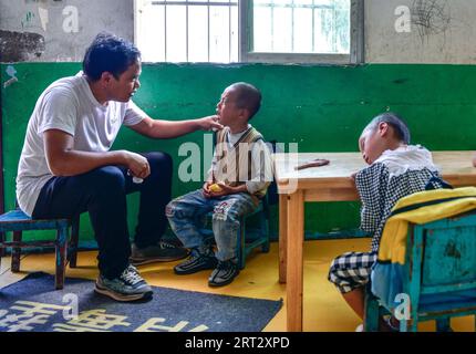 (230910) -- GUIDING, 10 septembre 2023 (Xinhua) -- lu Chengwen (1e L) apaise un élève d'âge préscolaire au point d'enseignement de Yanjiao dans le canton de Yanshan, dans le comté de Guizhou, dans le sud-ouest de la Chine, dans la province du Guizhou, 6 septembre 2023. Yanjiao point d'enseignement est une «micro école primaire» située dans une zone plate parmi les montagnes dans le sud-ouest de la Chine Guizhou. Lu Chengwen est le seul enseignant ici avec 28 élèves préscolaires et 6 élèves de première année. En 2012, lu, qui venait de sortir de l'université, choisit d'enseigner au point d'enseignement éloigné de Yanjiao. Élèves d'âge préscolaire, élevés dans le village montagneux de l'ethnie Miao Banque D'Images