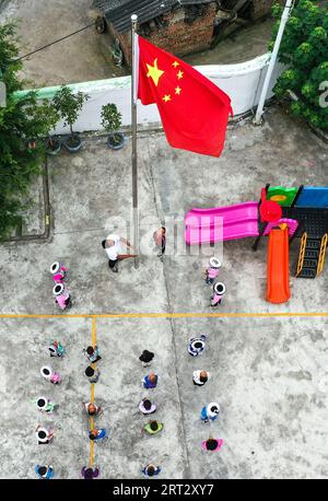 (230910) -- GUIDING, 10 septembre 2023 (Xinhua) -- cette photo aérienne prise le 7 septembre 2023 montre lu Chengwen et ses élèves assistant à une cérémonie nationale de levée de drapeau au point d'enseignement de Yanjiao dans le canton de Yanshan, dans le comté de Guizhou, dans le sud-ouest de la Chine. Yanjiao point d'enseignement est une «micro école primaire» située dans une zone plate parmi les montagnes dans le sud-ouest de la Chine Guizhou. Lu Chengwen est le seul enseignant ici avec 28 élèves préscolaires et 6 élèves de première année. En 2012, lu, qui venait de sortir de l'université, choisit d'enseigner au point d'enseignement éloigné de Yanjiao. Élèves préscolaires, Banque D'Images