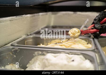 Main féminine prend la crème glacée du réfrigérateur avec pelle. Femme travaille dans le magasin de crème glacée. Concept de pâtisserie. Banque D'Images