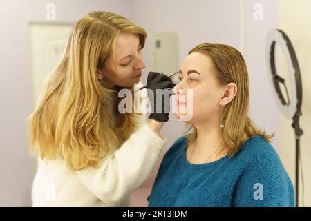 Le maître dessine la forme des sourcils avec de la peinture blanche avant la correction des sourcils. Industrie de la beauté. Banque D'Images