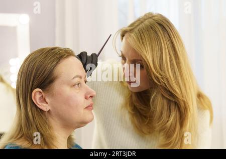 Le maître dessine la forme des sourcils avec de la peinture blanche avant la correction des sourcils. Industrie de la beauté. Banque D'Images