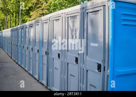 Rangée de toilettes publiques bleues et grises dans le parc par une journée ensoleillée Banque D'Images