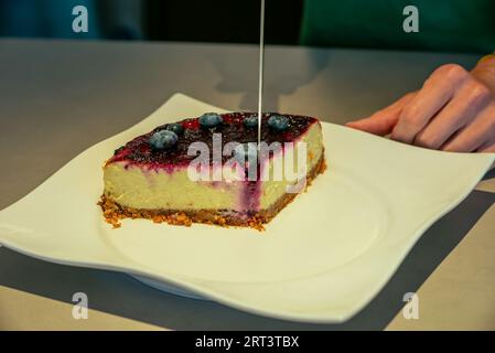 Une femme coupant un délicieux cheesecake blueberr dans un café Banque D'Images