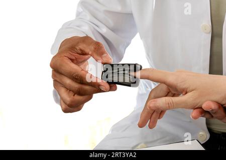 Médecin asiatique utilisant un sphygmo-oxymètre sur un doigt de femme européenne. Peau caucasienne, rousse. Cliché d'étude sur fond blanc Banque D'Images