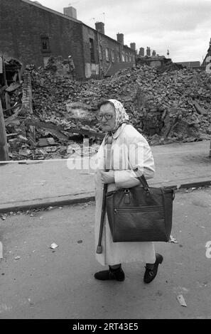 Toxteth Riots 1980s UK. Une femme du coin en train de faire du shopping passe devant des bâtiments incendiés qui ont été renversés pour être en sécurité après les émeutes un jour ou deux avant. Toxteth, Liverpool 8, Angleterre vers juillet 1981 HOMER SYKES Banque D'Images