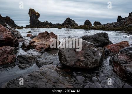 Bizarres formations rocheuses de lave noire et rochers de basalte volcanique dans les vagues sur la rive de la plage de Djúpalónssandur, Snæfellsnes, Islande Banque D'Images