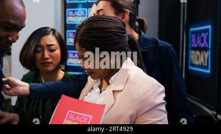 Les gens de la diversité folle à l'entrée du magasin deviennent fous pour les offres et les promotions du Black friday. Agent de sécurité afro-américain gérant le contrôle des foules pendant les ventes saisonnières à la boutique. Banque D'Images