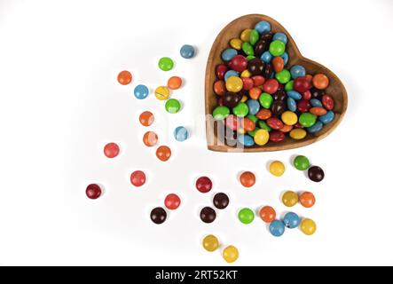 pile de bonbons au chocolat colorés dans un bol en bois en forme de coeur isolé sur fond blanc, vue de dessus Banque D'Images