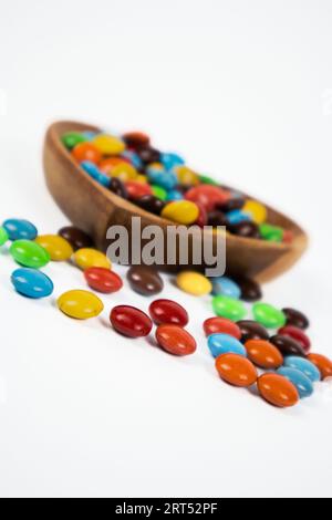 pile de bonbons au chocolat colorés dans un bol en bois sur fond blanc Banque D'Images