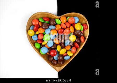 pile de bonbons au chocolat colorés dans un bol en forme de coeur sur fond noir et blanc, vue de dessus Banque D'Images