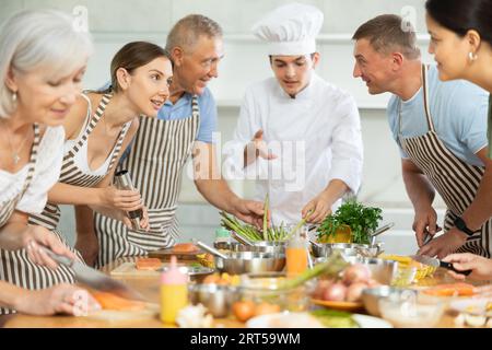 Chef en uniforme enseigne aux étudiants de cours de cuisine comment nettoyer et couper le filet de saumon Banque D'Images