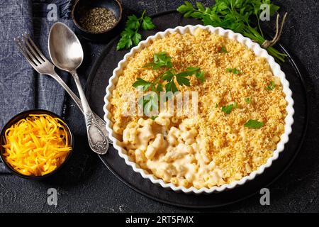 mac cuit au four et fromage saupoudré de chapelure panko et de persil frais dans un plat allant au four sur une table en béton avec fourchette et cuillère Banque D'Images