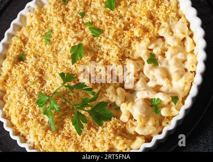 mac cuit au four et fromage saupoudré de chapelure panko et de persil frais dans un plat allant au four sur une table en béton, gros plan Banque D'Images