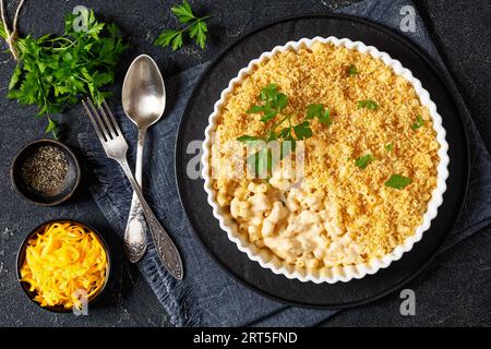 gros plan mac cuit au four et fromage saupoudré de chapelure panko et de persil frais dans un plat allant au four sur une table en béton avec des ingrédients, vue horizontale, f Banque D'Images