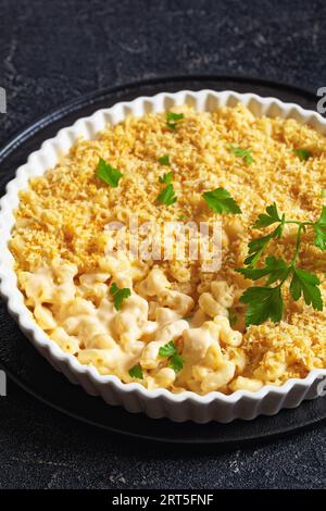 mac cuit au four et fromage saupoudré de chapelure panko et de persil frais dans un plat allant au four sur une table en béton, vue verticale, gros plan Banque D'Images