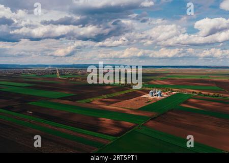 Silos de ferme dans le champ, vue aérienne du drone pov le jour ensoleillé de printemps avec des nuages blancs au-dessus de l'horizon Banque D'Images