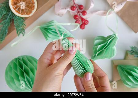 Les mains féminines déplient des ornements en nid d'abeille de Noël en papier. Décoration sans plastique pliable faite à la main. Concept d'artisanat de créativité hivernale. Mode éco DIY. SC Banque D'Images