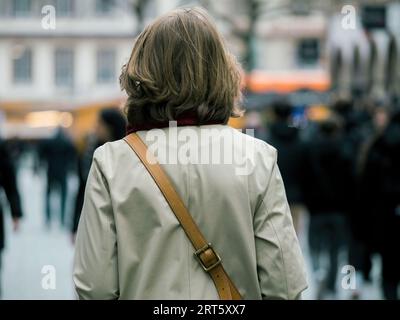 Une femme non identifiable est capturée par l'arrière, enfilée dans un trench coat, avec un fond de bokeh légèrement flou accentuant sa silhouette Banque D'Images