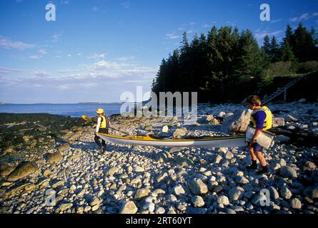 Deux femmes portent un kayak sur la plage, Muscongus Bay, Maine. Banque D'Images