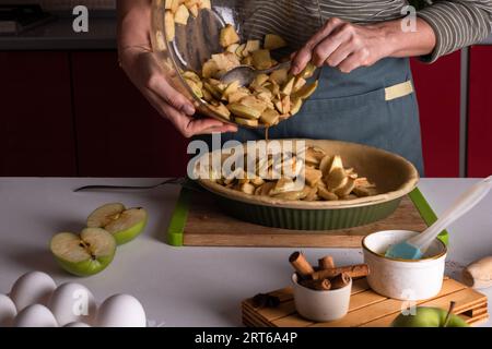 Femme versant des farces de pommes épicées pour la tarte aux pommes dans le plat de boulangerie avec de la pâte, processus de cuisson de style de vie, préparation de tarte de Thanksgiving, automne Banque D'Images