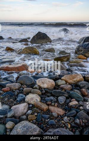 Vue du soir depuis la plage sur l'île de Jomfruland jusqu'à une mer relativement calme avec des vagues douces qui se brisent et des rochers humides et scintillants. Telemark, Norvège. Banque D'Images