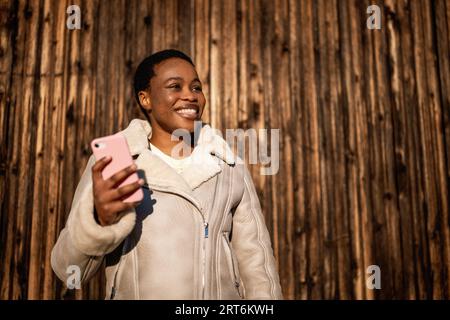 Portrait en plein air d'une femme afro-américaine heureuse. Elle est en messagerie sur smartphone. Banque D'Images