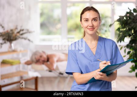 Souriant jeune physiothérapeute féminin remplissant des formulaires médicaux dans le studio de bien-être Banque D'Images