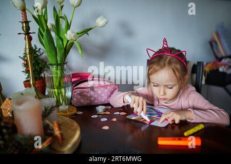 Adorable fille d'enfant d'âge préscolaire avec la peinture de décoration de cheveux licorne utilisant le stylo feutre à la maison. Activités créatives intérieures pour les enfants Banque D'Images