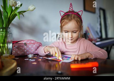 Adorable fille d'enfant d'âge préscolaire avec la peinture de décoration de cheveux licorne utilisant le stylo feutre à la maison. Activités créatives intérieures pour les enfants Banque D'Images