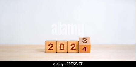 2024 bonne année avec changement aux concepts de nouvelle ère. Retournement des numéros de calendrier de 2023 à 2024 ans sur des blocs de cube en bois isolés sur la table en bois et Banque D'Images